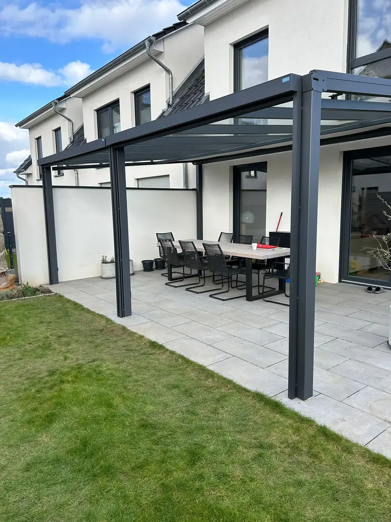 Anthrazitfarbenes Terrassendach mit Glas an einer Doppelhaushälfte, darunter Tisch und Stühle