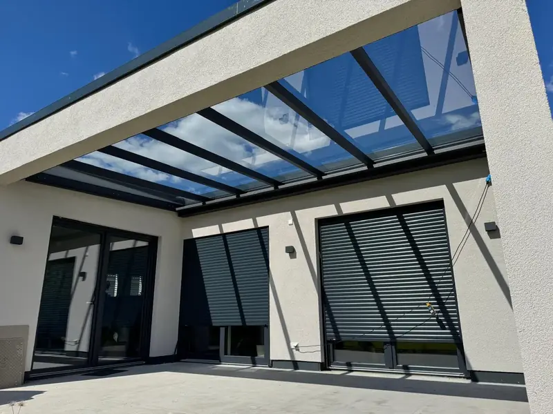 Blick von unten auf ein Terrassendach mit klarem Glas an einem verputzten Haus